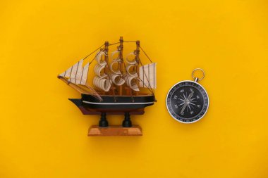 Minimalizm yolculuğu, macera düzlüğü. Sarı arka planda pusula ve gemi. Üst görünüm