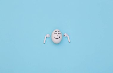 Tavuk yumurtası gülen surat mavi arka planda kablosuz kulaklıkla müzik dinle.
