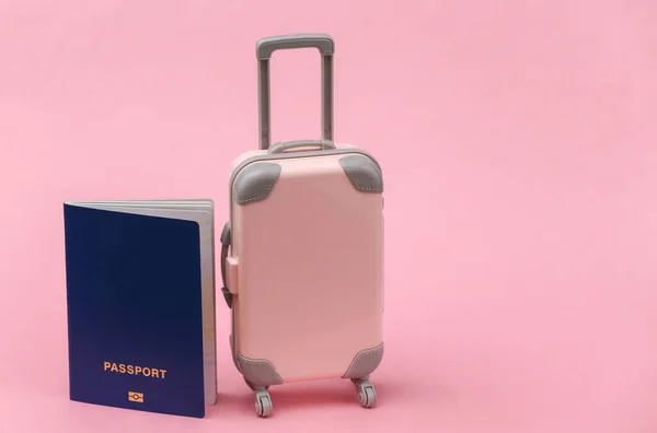 International travel concept. Mini  plastic travel suitcase with passport on pink background.