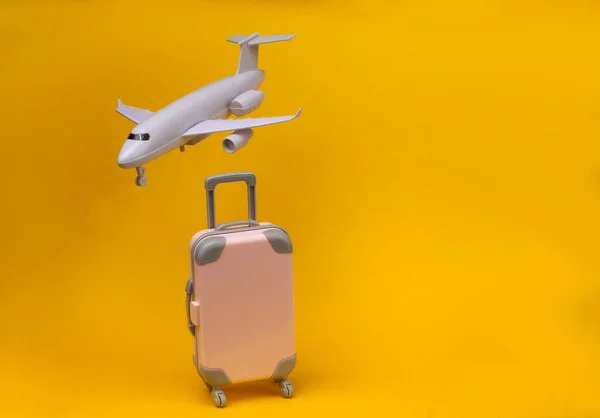 Air travel concept. Mini plastic travel suitcase, air plane on yellow  background.