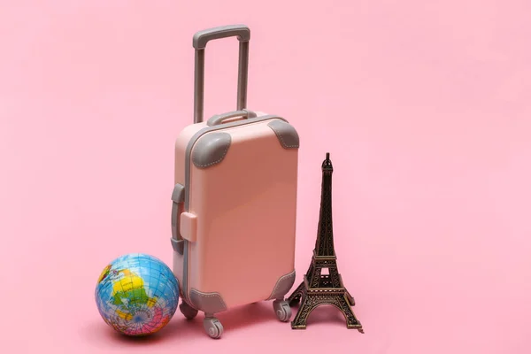 Traveled to Paris. Mini plastic travel suitcase and statuette of the Eiffel Tower, globe on pink background.