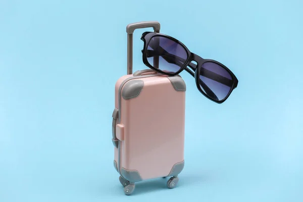 Travel or trip concept. Mini plastic travel suitcase with sunglasses on blue background. Minimal style