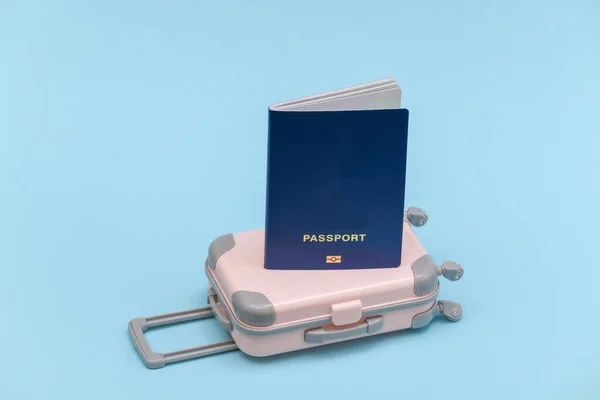 Travel or trip concept. Mini plastic travel suitcase with passport on blue background. Minimal style