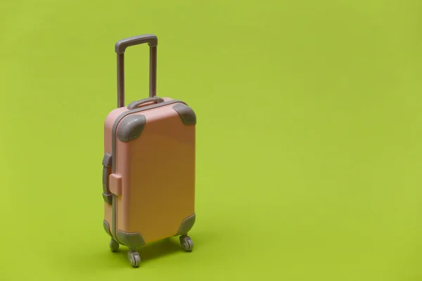 Travel or trip concept. Mini plastic travel suitcase on green background. Minimal style