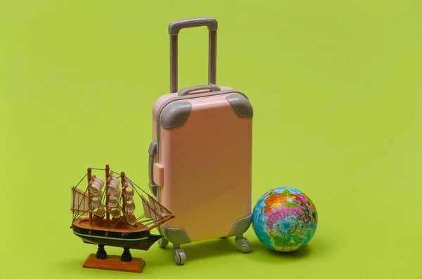Travel concept. Mini plastic travel suitcase and globe, ship on green background. Minimal style