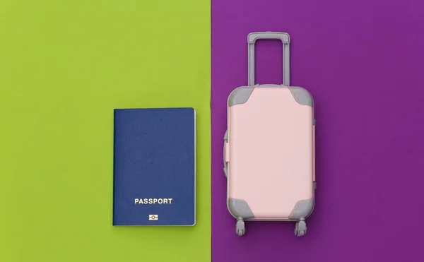 Travel flat lay. Mini plastic travel suitcase, passport on green purple background. Minimal style. Top view