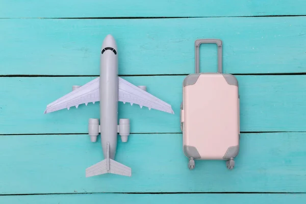 Flat lay vacation holiday and travel planing concept. Mini plastic travel suitcase and air plane on blue wooden background. Top view