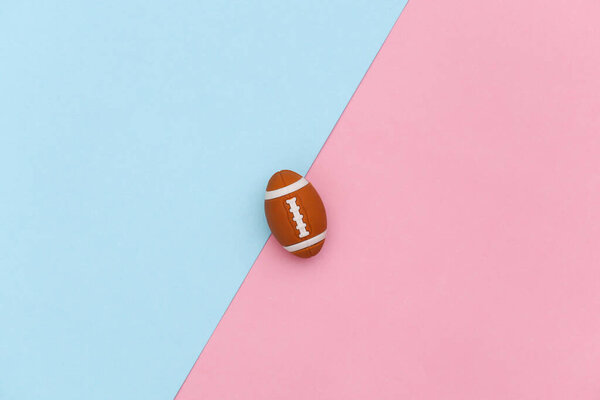 Мини регби мяч на сине-розовом пастельном фоне. Концепция минимализма. Вид сверху. Плоский лежал