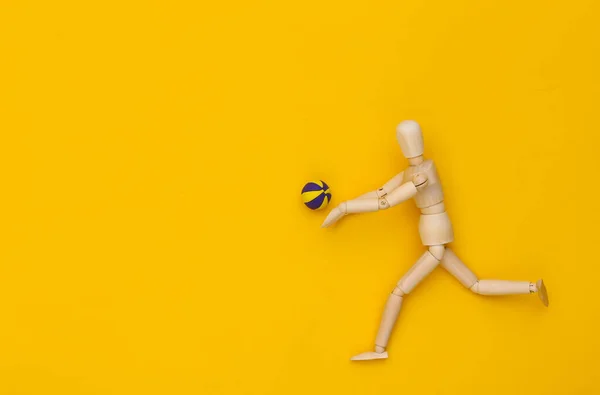 Wooden puppet plays volleyball with ball on yellow background