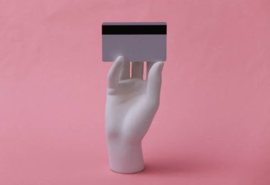 Beyaz mankenin elinde pembe arka planda bir banka kartı var. Alışveriş, kredi, online para