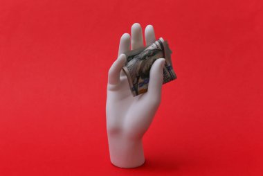 Beyaz manken elinde kırmızı arka planda 100 dolarlık banknotlar tutuyor.