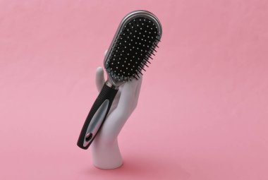 Saç fırçalı beyaz manken el pembe arka planda duruyor. Saç bakımı, güzellik konsepti