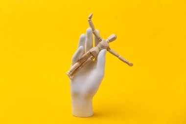 Beyaz manken el sarı arka planda tahta kukla tutuyor.