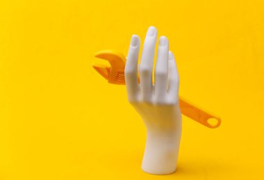 Sarı arka planda İngiliz anahtarı beyaz mankenin elinde. Yenileme konsepti, endüstri. Minimalizm