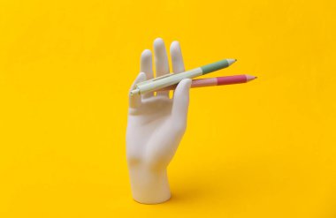 Beyaz mankenin elinde mavi arka planda kalemler var.