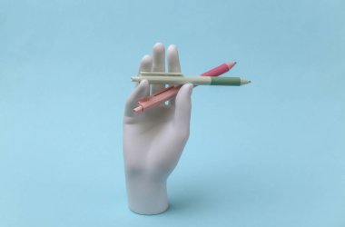 Beyaz mankenin elinde mavi arka planda kalemler var.