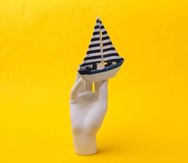 Beyaz manken, sarı arka planda kayığı tutuyor. Seyahat kavramı