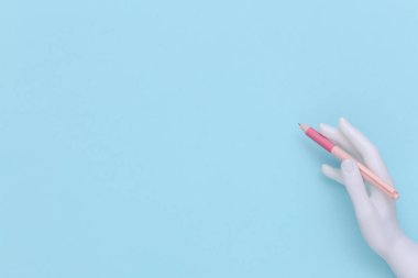 Manken el, mavi arkaplanda fotokopi alanı olan bir kalem tutuyor. Üst görünüm