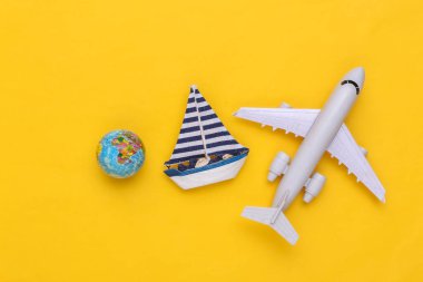 Yelkenli ve uçak, sarı arka planda dünya. Seyahat minimalizmi konsepti. Üst Manzara. Düz yatıyordu