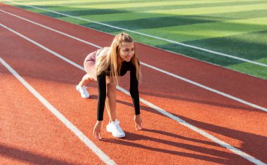 Genç ve formda bir kadın stadyumda düşük başlangıç koşusuna hazırlanıyor.