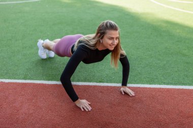 Genç, sıska kadın dışarıda şınav çekiyor.