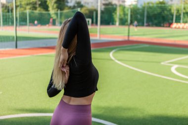 Spor kıyafetleri içinde formda bir kadın ısınma antrenmanı yapıyor, stadyumda el esneme hareketleri yapıyor. Sağlıklı yaşam tarzı kavramı. Açık hava eğitimi