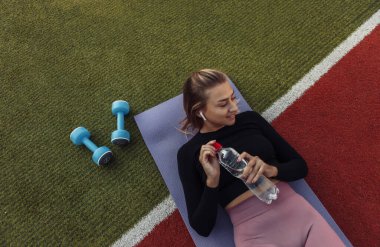 Sağlıklı, genç bir kadın paspasın üzerinde dinleniyor. Açık hava eğitimi. Spor, spor konsepti. Sağlıklı yaşam tarzı