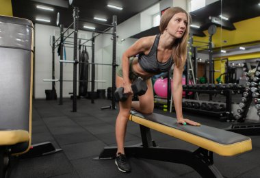 İnce, fit bir kadın spor salonundaki bir eğimde halterleri kaldırma alıştırması yapıyor. Sağlıklı bir yaşam tarzı. Vücut geliştirme ve Fitness