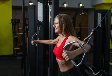 Spor makinesinde kaslarını esneten sağlıklı bir kadın. Modern jimnastik salonunda egzersiz makinesi kablolu yayınıyla egzersiz yapan bir kız. Fitness ve vücut geliştirme
