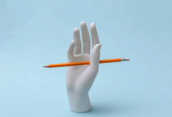 White mannequin hand with pencil stands on blue background. Knowledge, education concept