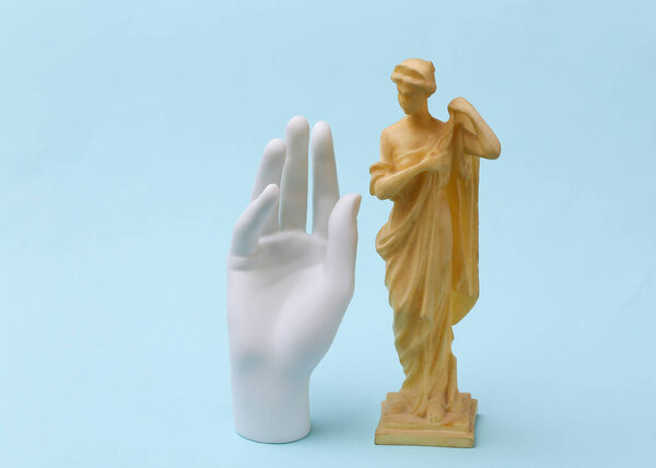 Рука из гипса и старинная статуя на синем фоне.