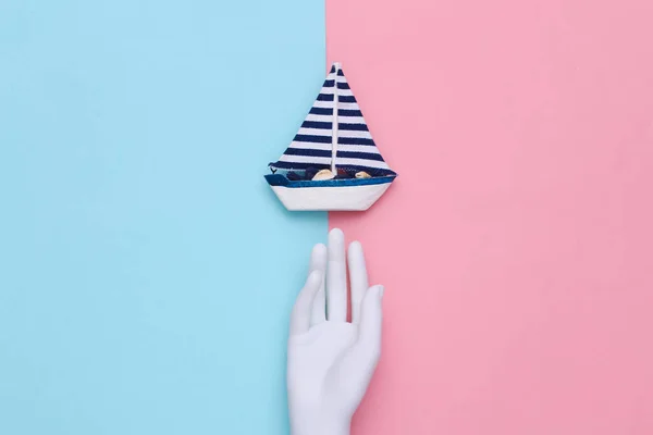 White mannequin hand and boat on blue pink background. Travel concept. Top view