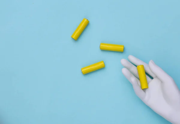 White mannequin hand holds AA type batteries on a blue background. Top view