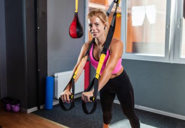 Uzaklaştırma kayışları eğitimi. Gülümseyen sporcu kadın spor salonunda kemerleriyle antrenman yapıyor. 