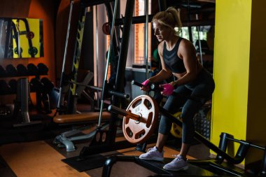 Formda bir kadın spor salonunda T-bar kürek egzersizi yapıyor.