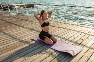 Spor yapan kadın plajda dinleniyor, gün doğumunda kulaklıkla müzik dinliyor.