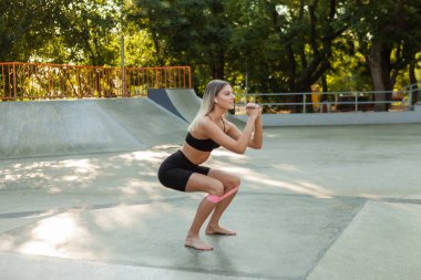Güzel, formda bir kadın sabah egzersizi yapıyor. Açık havada lastik bantlarla..