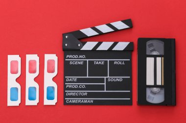 Alkış tahtası, 3D gözlükler, kırmızı arka planda video kaset. Üst görünüm