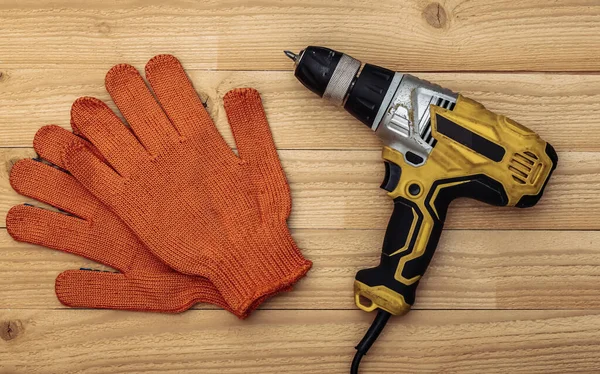 Old drill screwdriver and work gloves on a wooden background. Top view