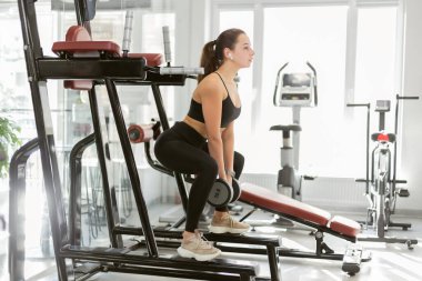 Genç fitness kadını halterle egzersiz yapıyor, spor salonunda bacak kaslarını çalıştırıyor.