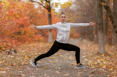 Genç çekici kadın sonbahar ormanında yoga yapıyor. Savaşçı 2 pozisyonu. Sağlıklı yaşam tarzı