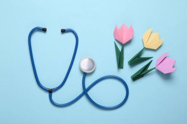 Mavi arka planda steteskop ve origami laleleri. Sıhhiye günü, tatil, üst manzara