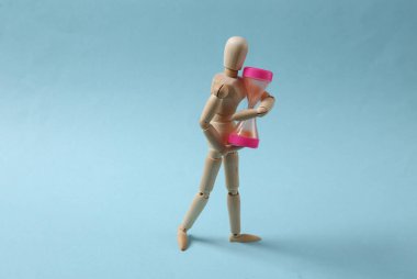 Mavi arka planda kum saati tutan tahta kukla.