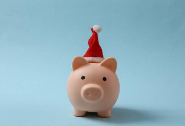 Mavi arka planda Noel Baba şapkası olan bir kumbara. Noel konsepti