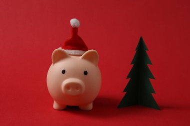 Noel Baba şapkası ve kırmızı arka planda Noel ağacı olan bir kumbara. Noel konsepti