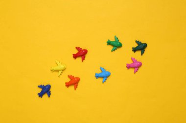Sarı arka planda bir sürü renkli oyuncak uçak. Seyahat kavramı