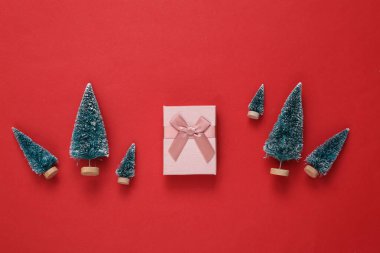 Kırmızı arka planda hediye kutusu olan mini Noel ağaçları. Yeni yıl ya da yılbaşı geçmişi. Üst Manzara. Düz yatıyordu