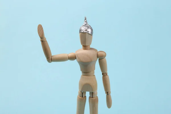 Mavi arka planda folyo şapkalı tahta kukla. Komplo