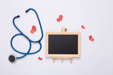 Fotokopi alanı olan küçük boş tebeşir tahtası ve beyaz arka planda kalpleri olan steteskop. Tıp konsepti