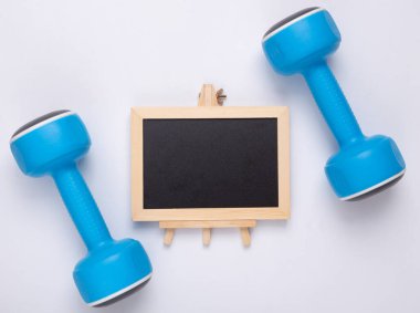 Beyaz arka planda dambıllar olan küçük bir kara tahta. Kopya alanı olan tebeşir tahtası. Spor ve spor konsepti